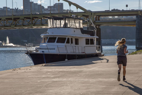 A woman jogs on the Three Rivers Heritage Trail next to a docked boat.