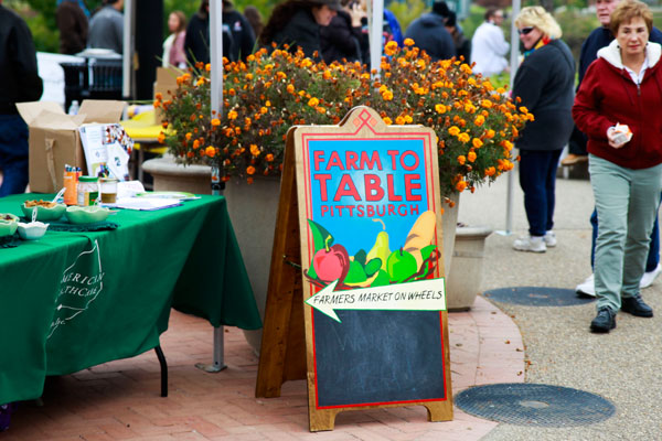 A sign saying "Farm to Table" with an arrow sits on the piazza next to an planter full of orange flowers.