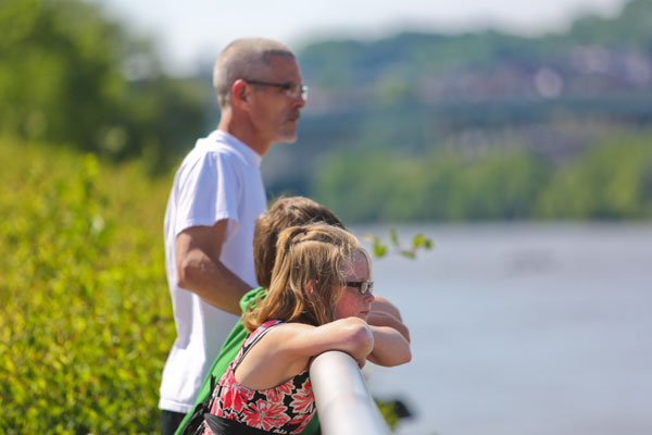 A father and two children look out over a railing at the river.
