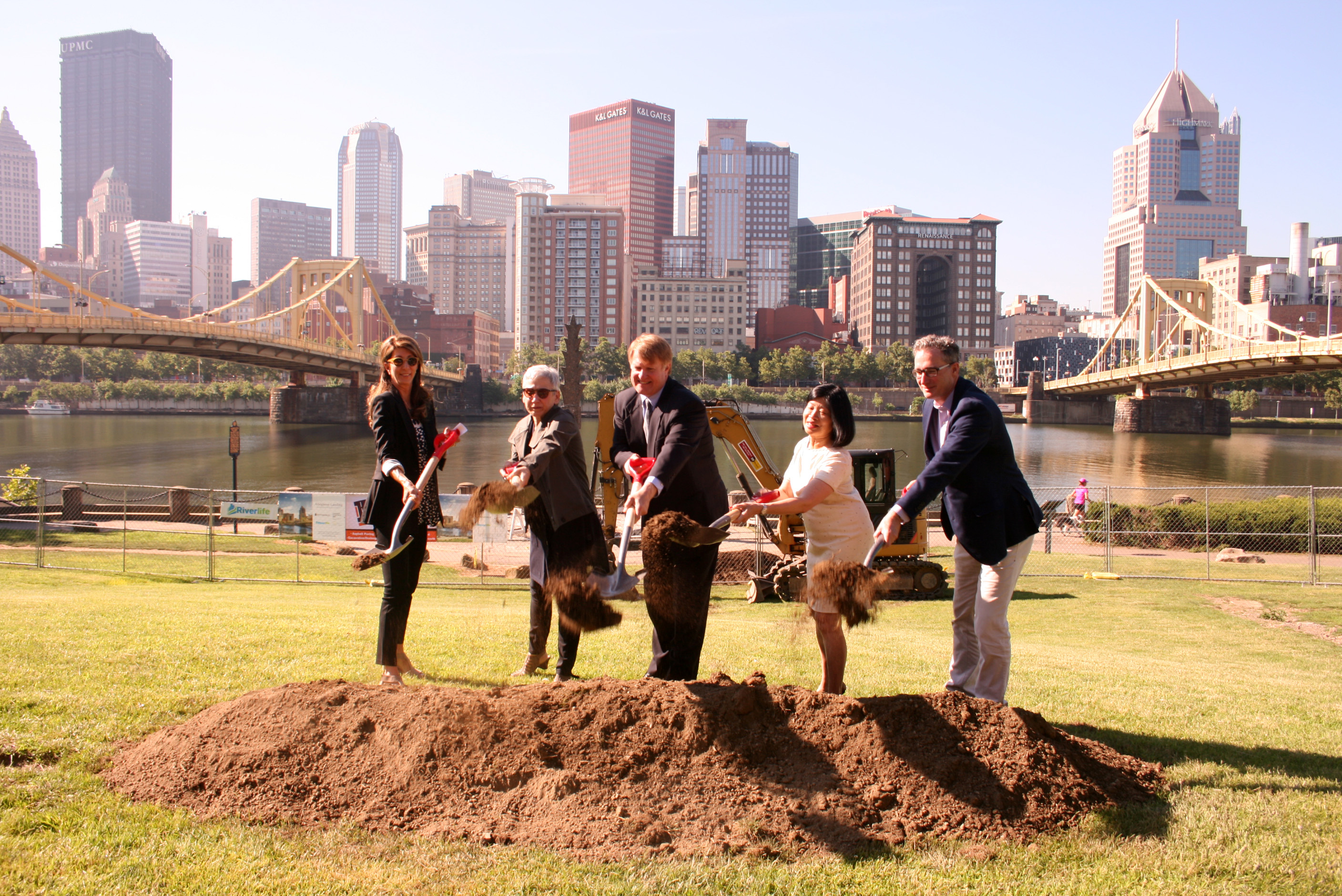 Officials break ground on Allegheny Landing with the city skyline behind them.