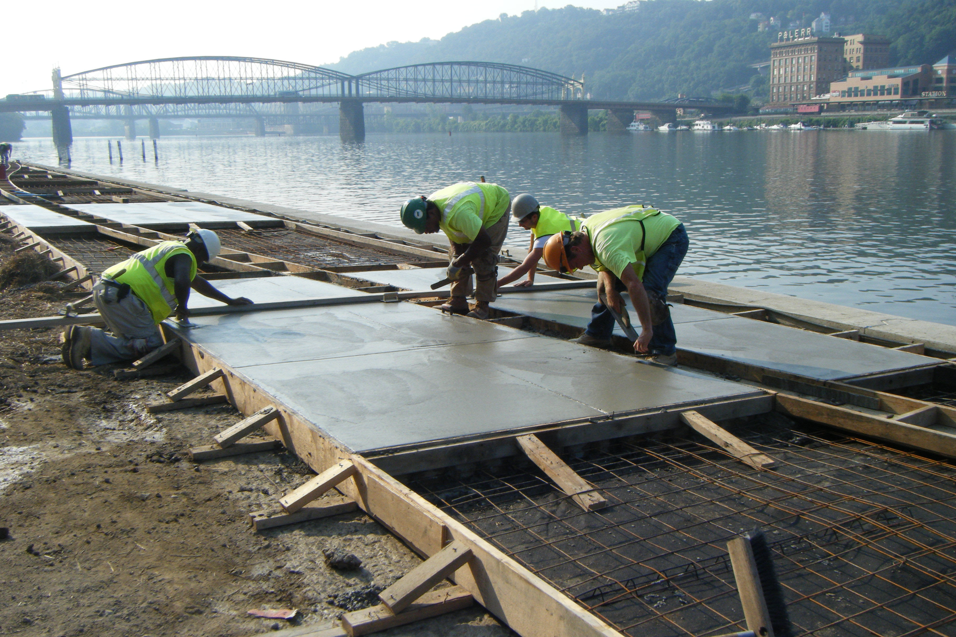 Construction workers pour cement on the Mon Wharf next to the river.