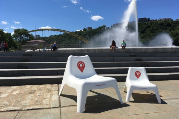 One big and one little white plastic chair sit next to the Point State Park fountain