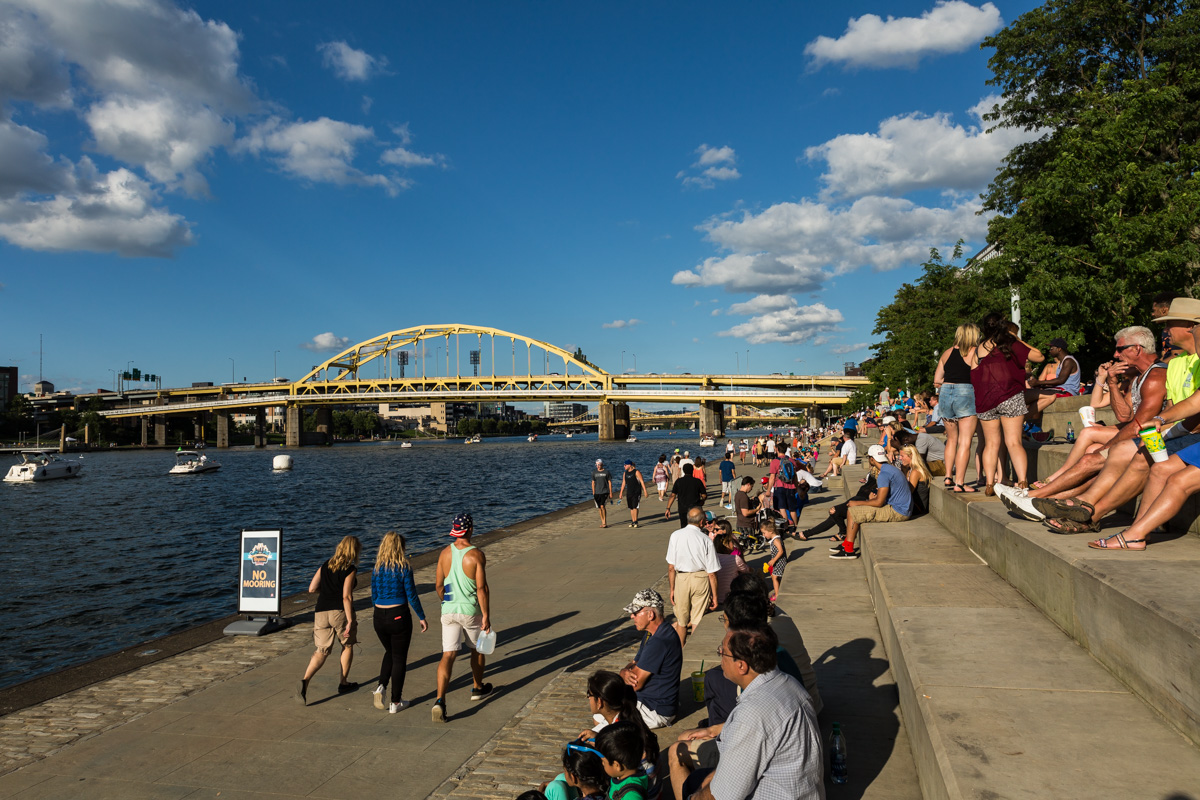 People sit facing the river on the steps of the Point State Park promenade.