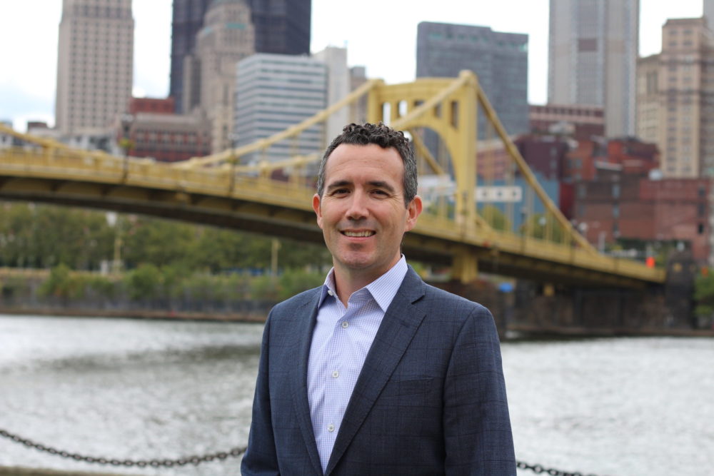 Matt Galluzzo in foreground with yellow 6th Street Bridge and Pittsburgh skyline in background